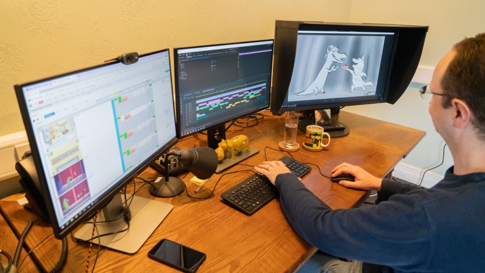 An individual sits in front of three computer screens. The images on the screen suggests the work involves editing. 