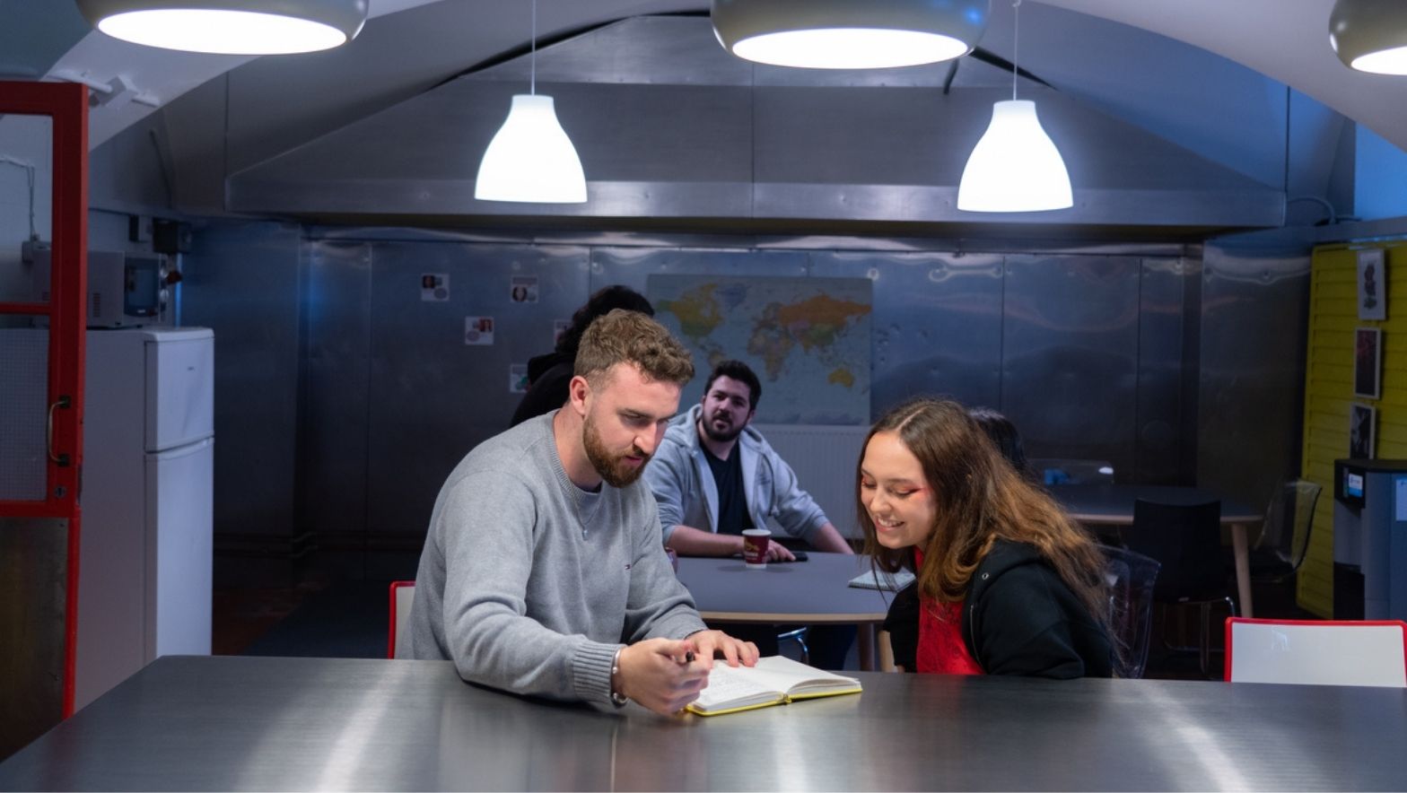 Two people are seated, looking at something. There are two overhead lights. 