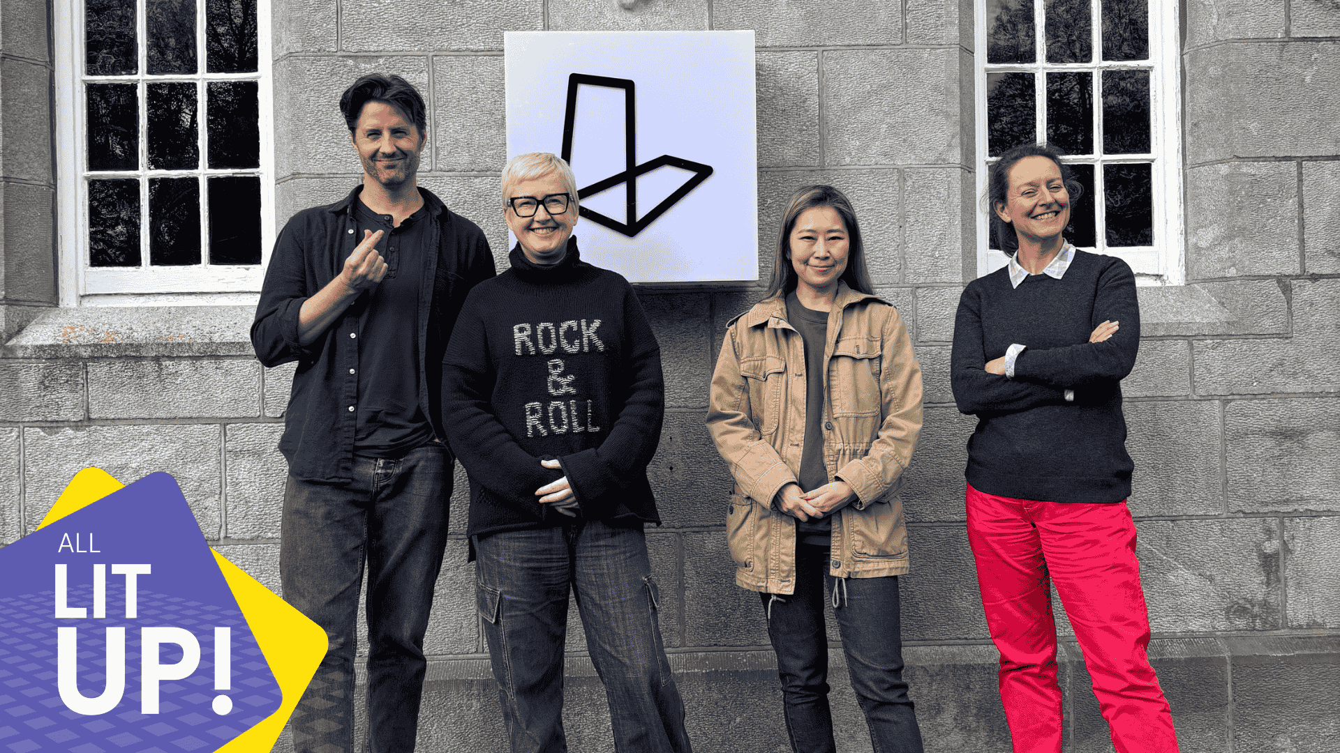 Four smiling individuals pose in front of a lightbox that displays the logo for Lighthouse Studios. In the corner is a graphic logo containing the words 'All Lit Up!' representing the logo for the studio's podcast.