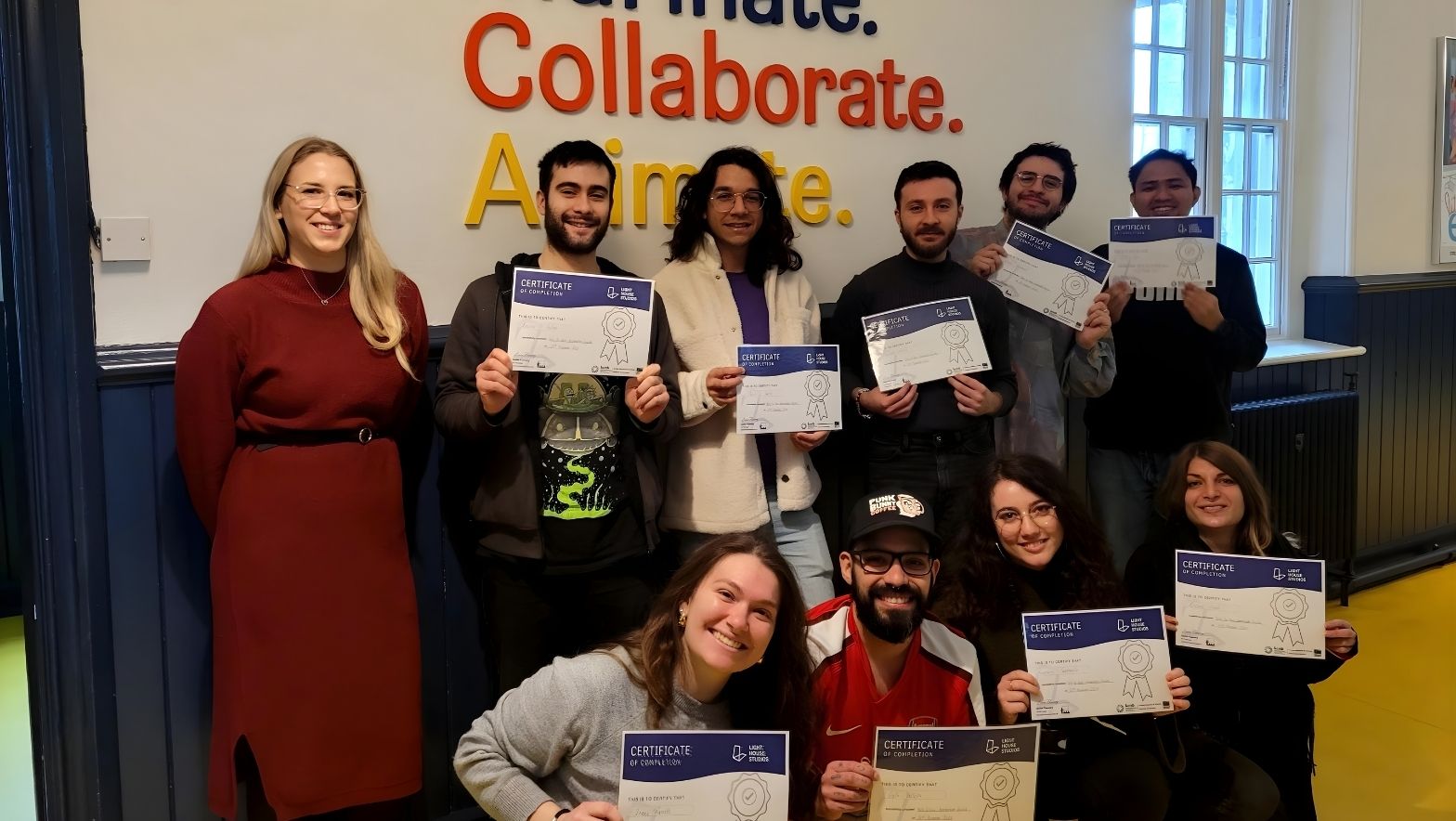 A group of individuals holding certificates pose in front of a colourful sign