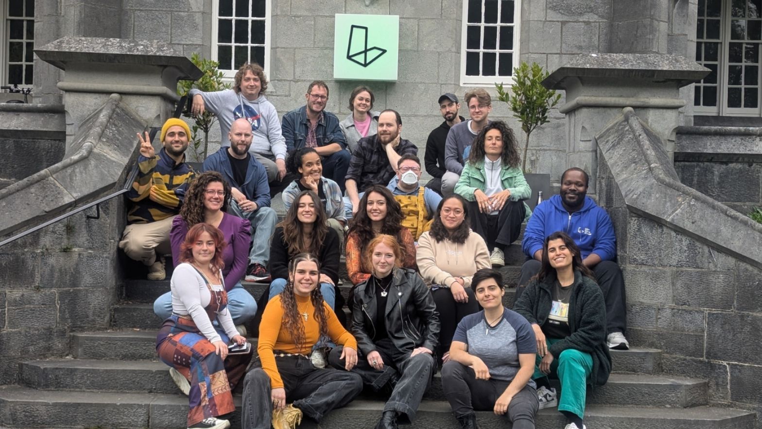 A diverse group of people sitting and smiling for the camera, on steps in front of a building.