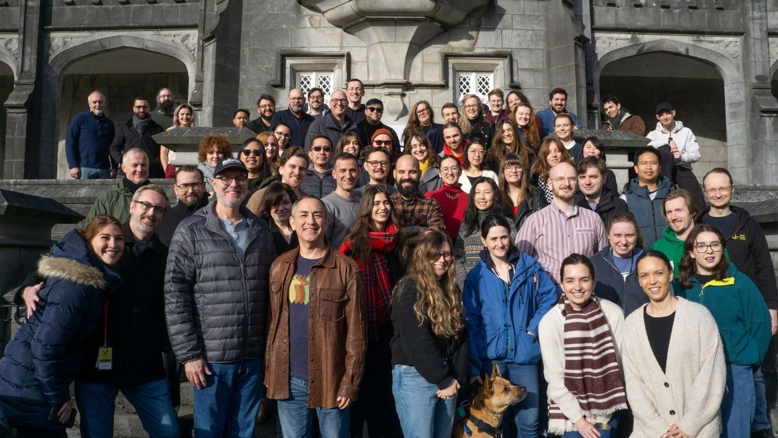 A diverse group of people smiling and standing together in front of a large building.