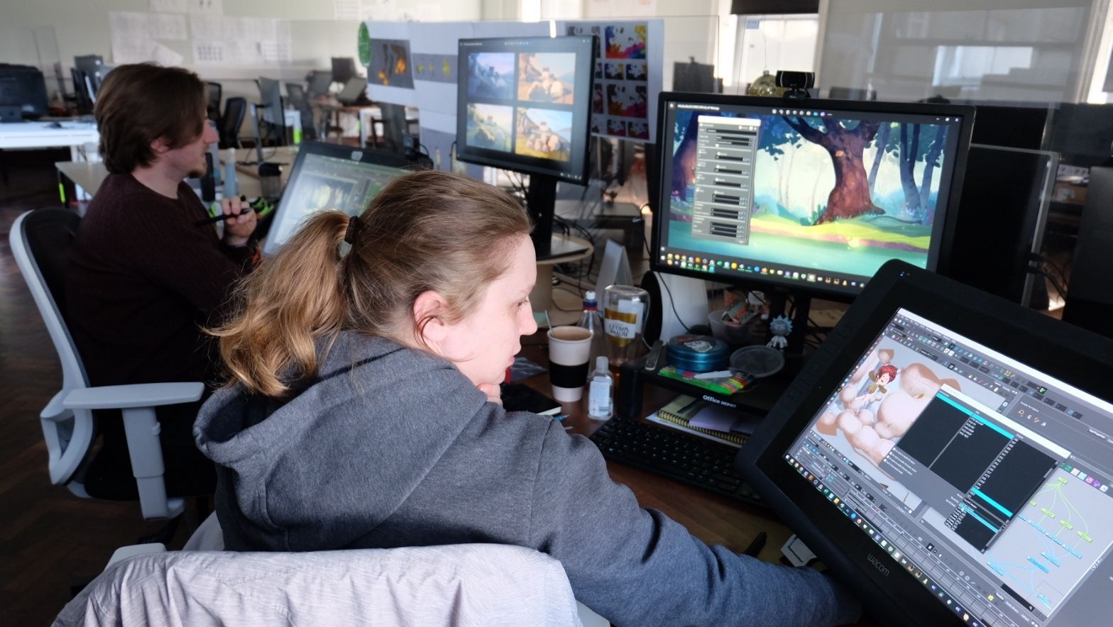 A person sits at a computer screen. There are multiple screens with different images. The individual appears to be working. 